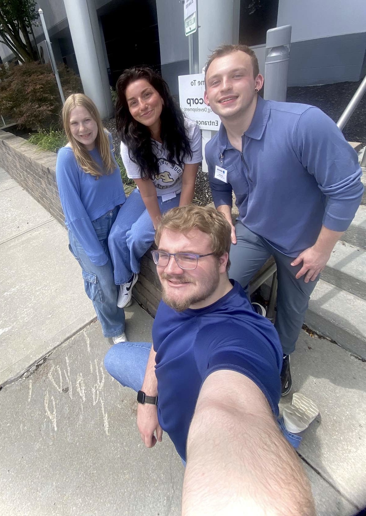 A group of four individuals posing for a selfie in front of stairs.