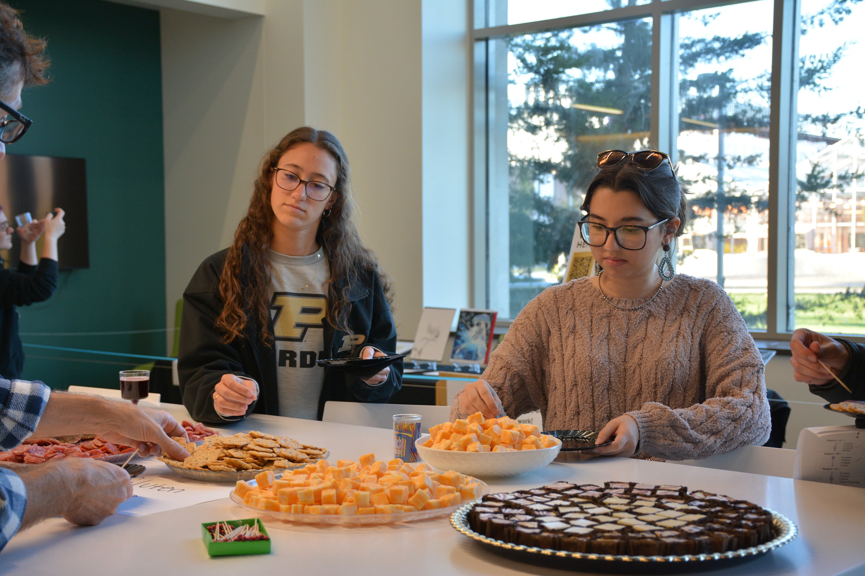 Students enjoy snacks during the Purdue Animal Sciences Art Show reception in Creighton Hall. Tables are filled with cheese, crackers, and desserts as attendees mingle and view the artwork displayed nearby.