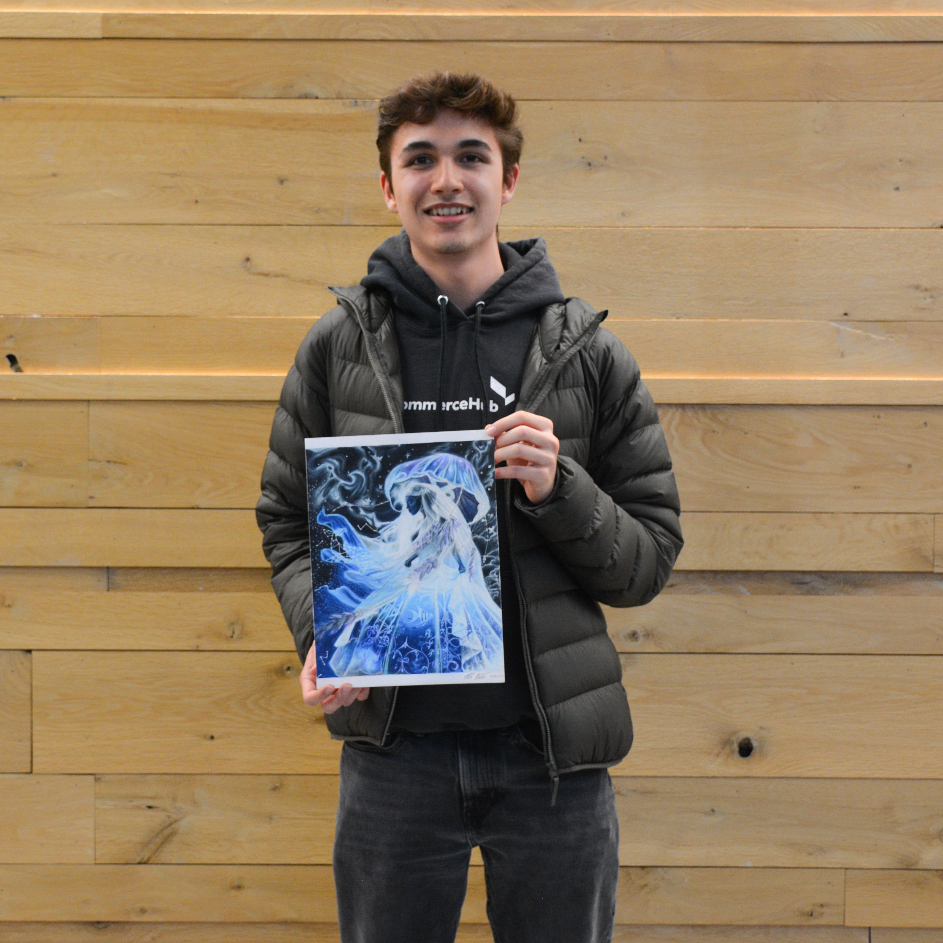 Colin Newton holds his detailed blue-toned drawing that won in the Drawing category of the Purdue Animal Sciences Art Show. He stands in front of a light wood wall inside Creighton Hall, smiling for the photo.
