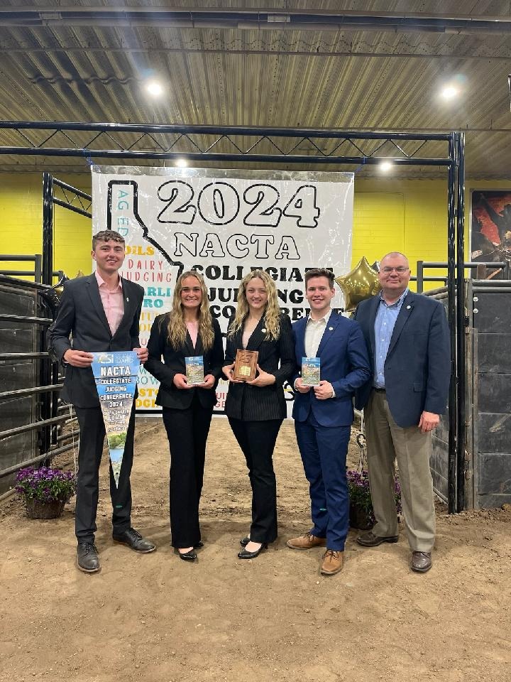 Brian Engleking and the 2024 Purdue Dairy Judging Team pose together inside an arena, holding awards and a banner from the 2024 NACTA Collegiate Judging Conference.