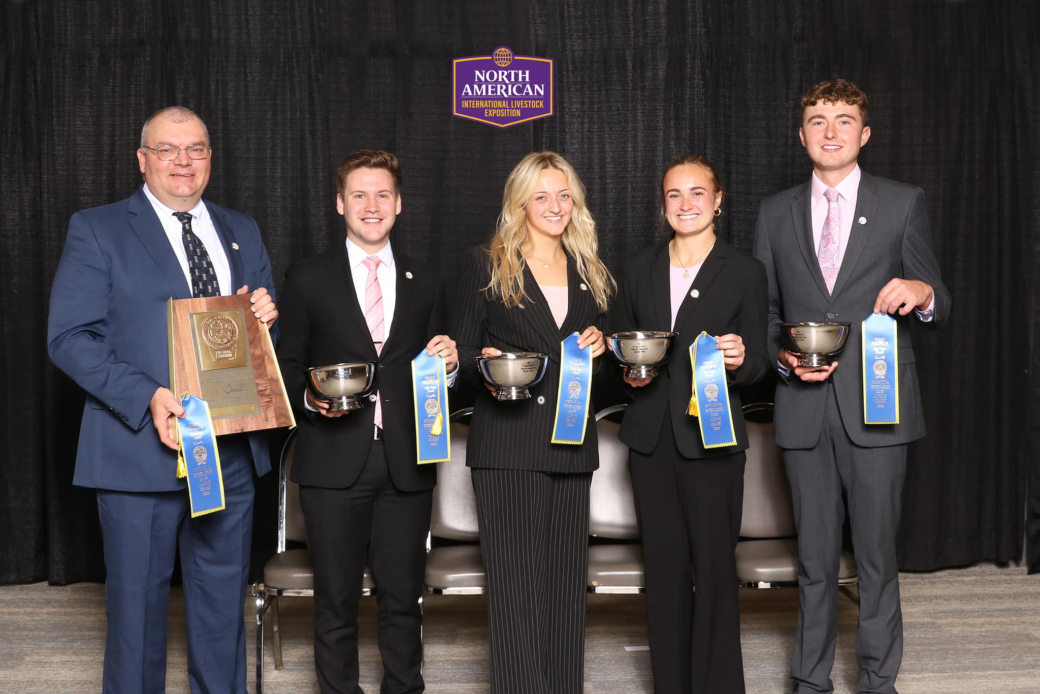Brian Engleking and four members of the 2024 Purdue Dairy Judging Team stand in front of a black backdrop holding blue ribbons, trophies, and a large team plaque from the North American International Livestock Exposition.