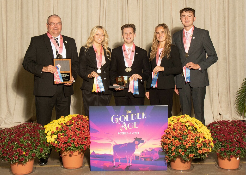 Brian Engleking stands with four members of the 2024 Purdue Dairy Judging Team behind a sign reading “The Golden Age.” The group holds medals and blue ribbons earned at a fall competition.