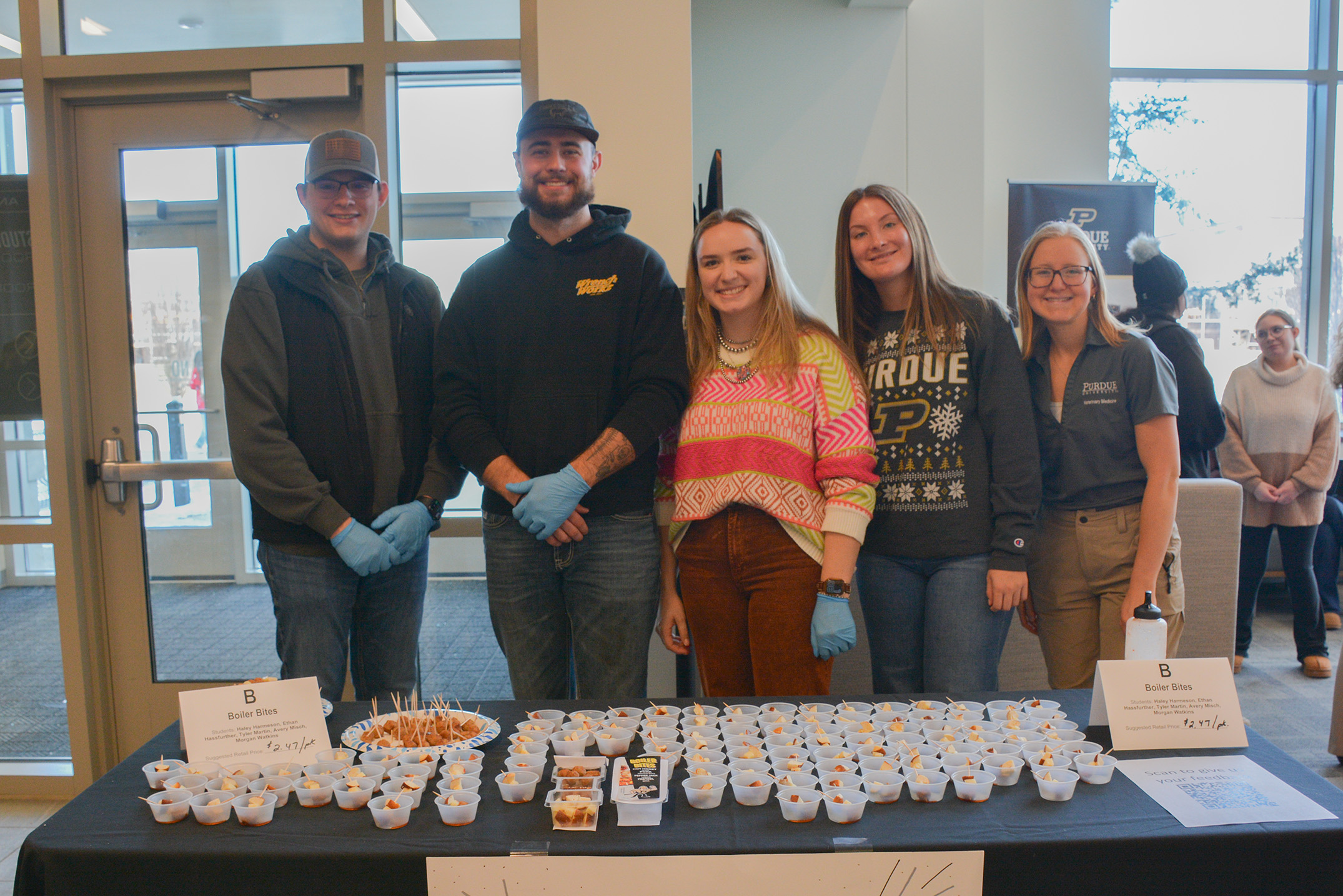 ANSC 360 students stand behind a display table filled with sample cups of their Boiler Bites product at the Purdue Animal Sciences product show.