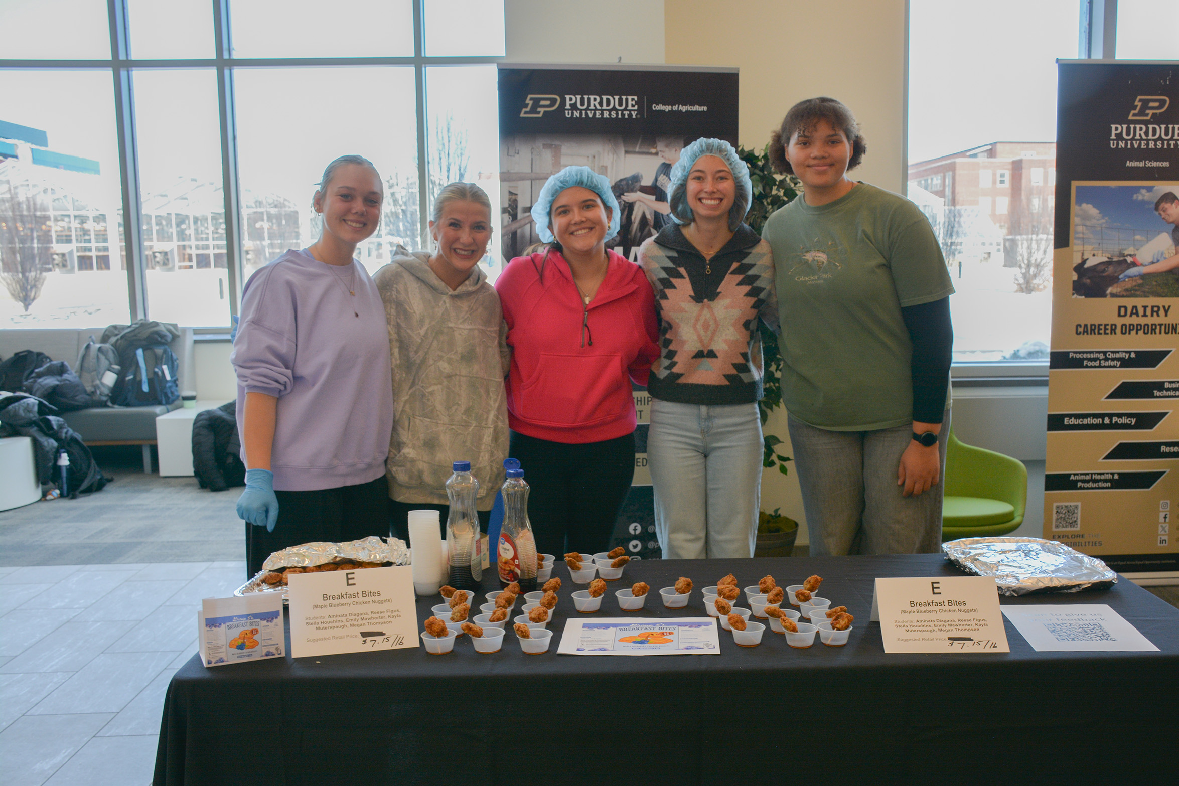 Students stand behind a display table presenting their Breakfast Bites, with sample cups of maple blueberry chicken nuggets and product signage at the ANSC 360 Product Show.
