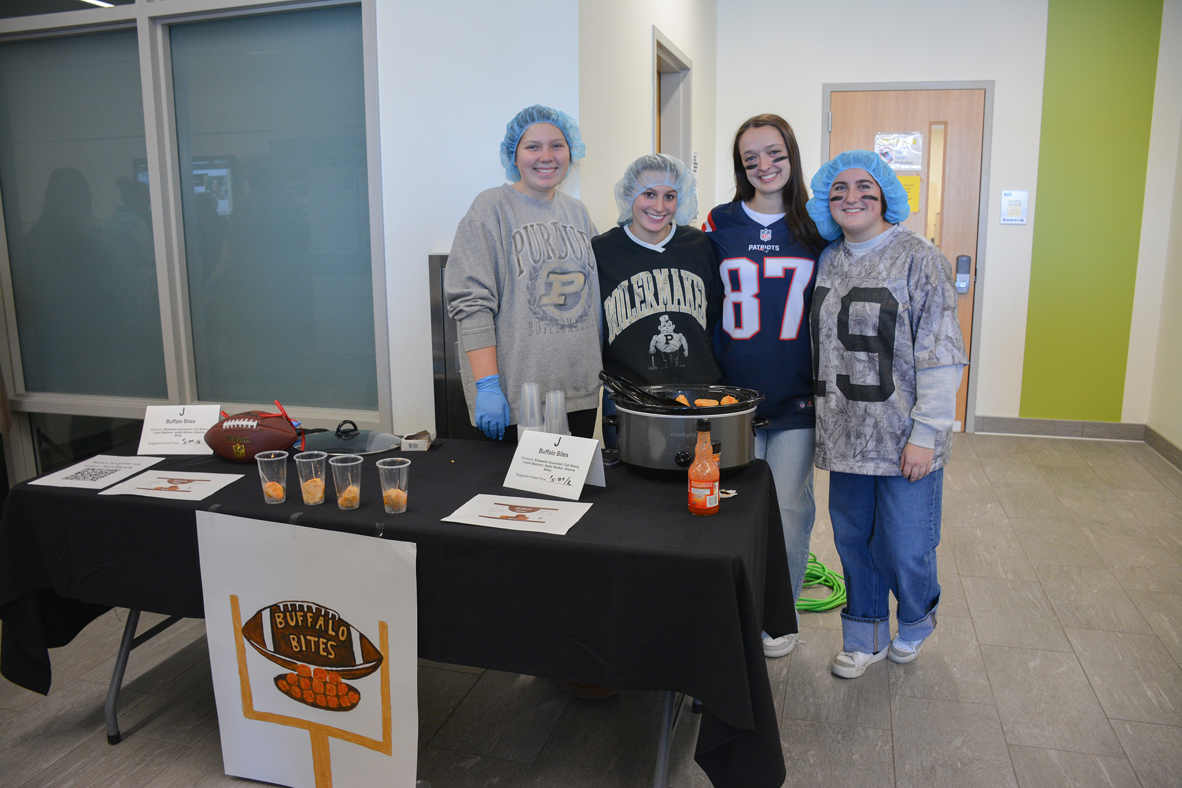 Students stand behind a display table presenting their Buffalo Bites, with sample cups, a slow cooker and product signage during the ANSC 360 Product Show.