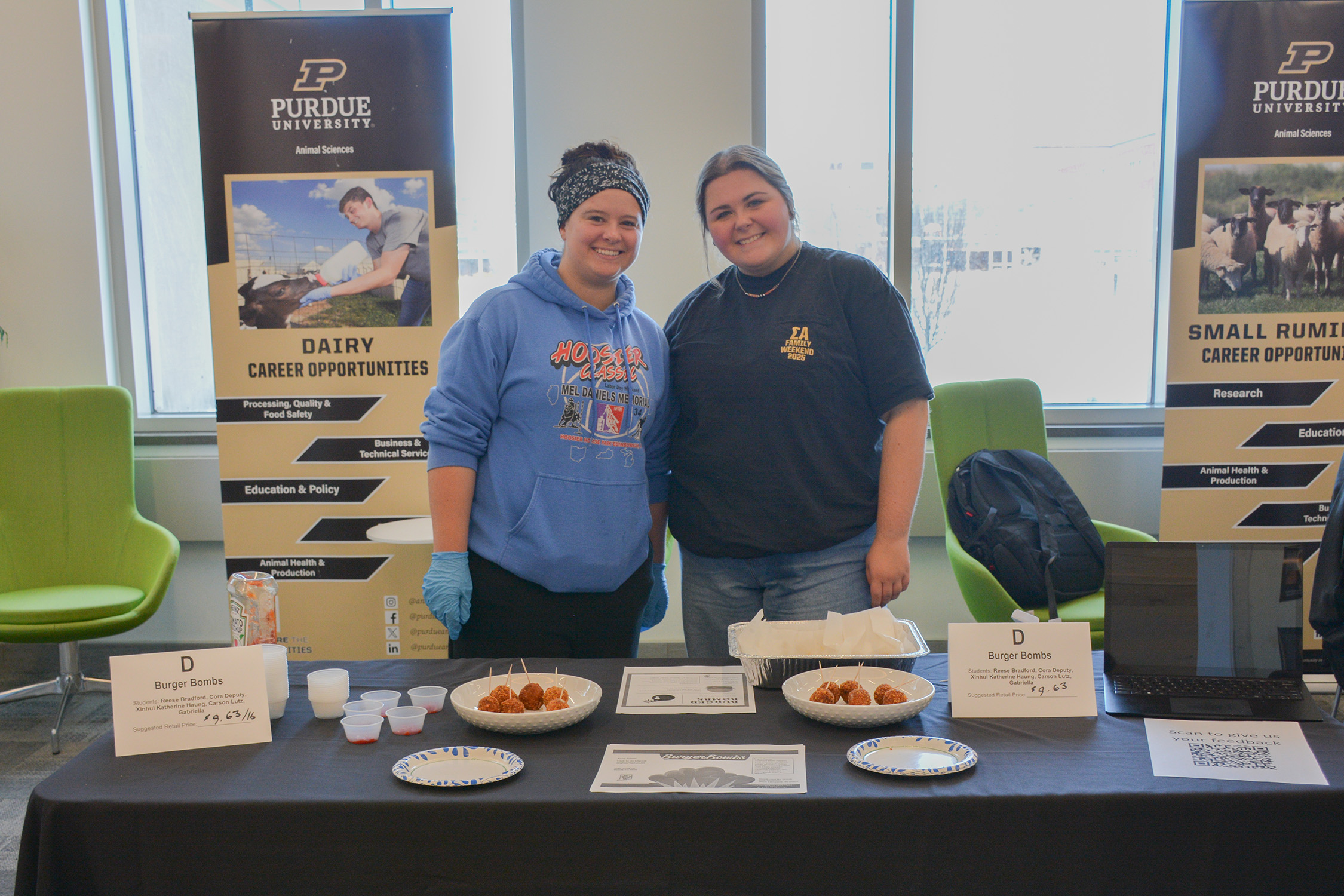 Students stand behind a display table presenting their Burger Bombs, with plated samples and product signage during the ANSC 360 Product Show.