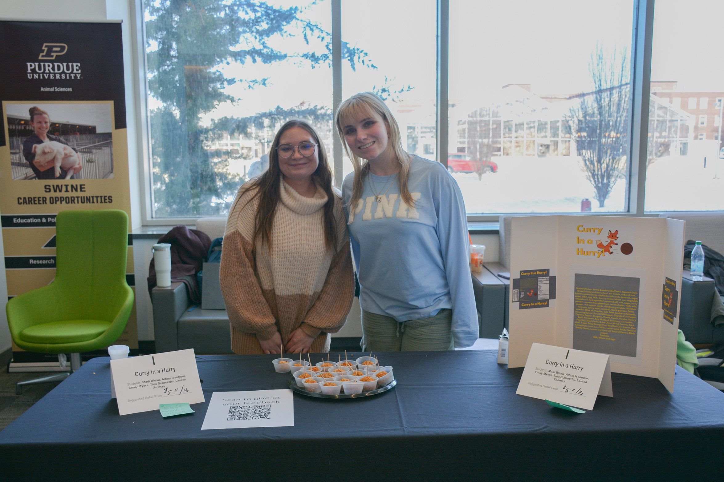 Students stand behind a display table presenting their Curry in a Hurry product, with sample cups of chicken curry meatballs and product signage at the ANSC 360 Product Show.