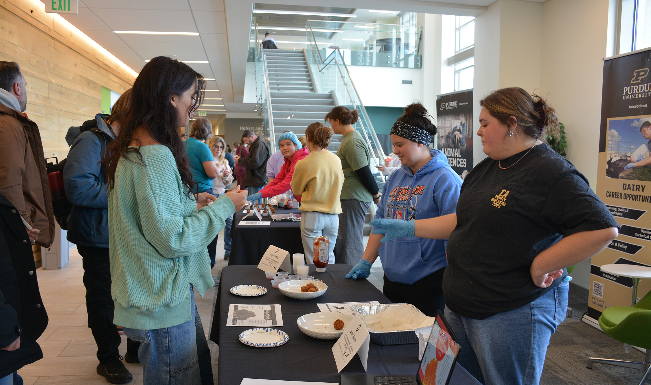 Students in the ANSC 360 Product Show stand behind display tables, offering samples of value-added meat products and speaking with attendees in the lobby of Creighton Hall.
