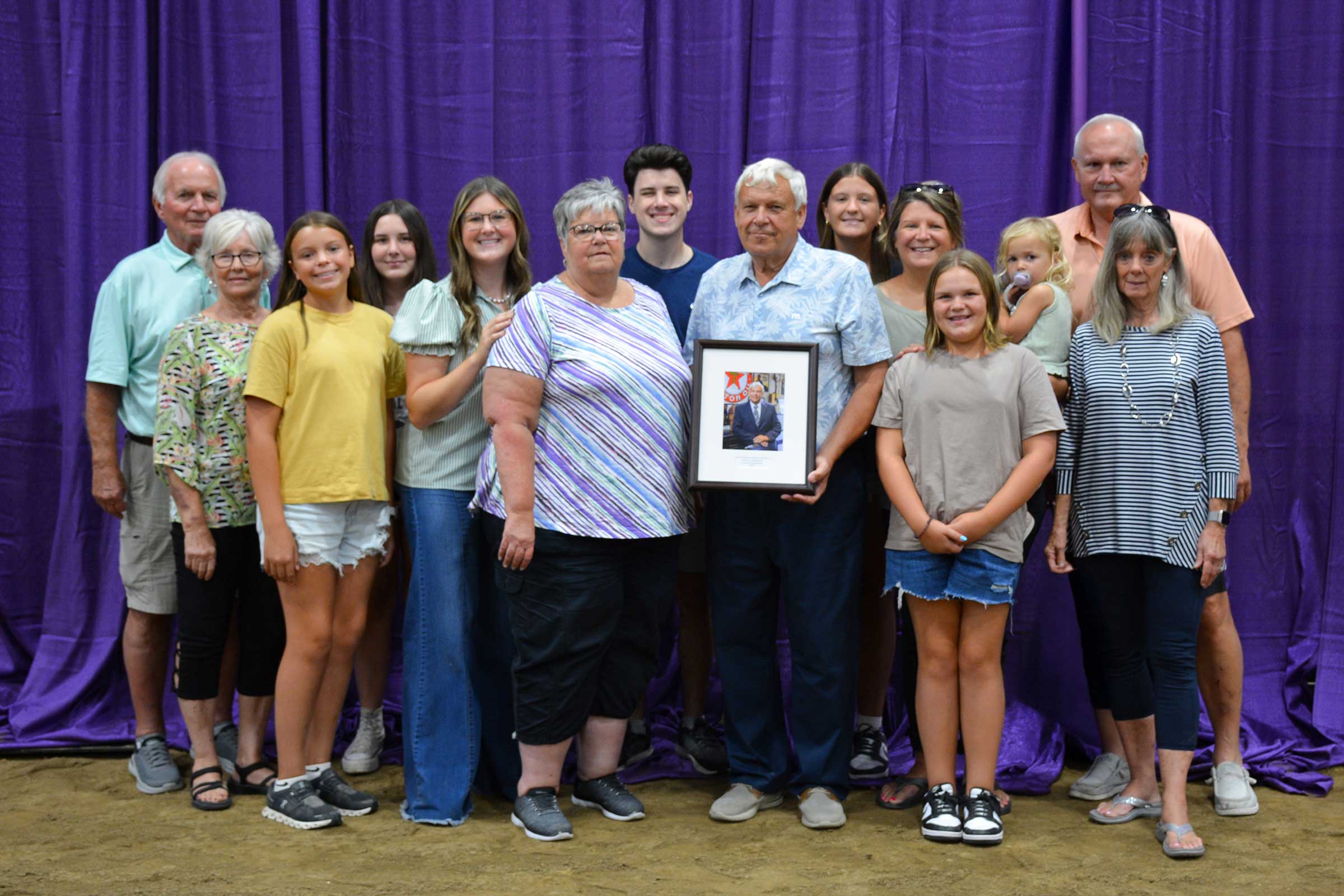 Keith Lambright poses with family and friends while holding his Hall of Fame portrait following his induction into the Indiana Livestock Breeders Association Hall of Fame at the Indiana State Fair.