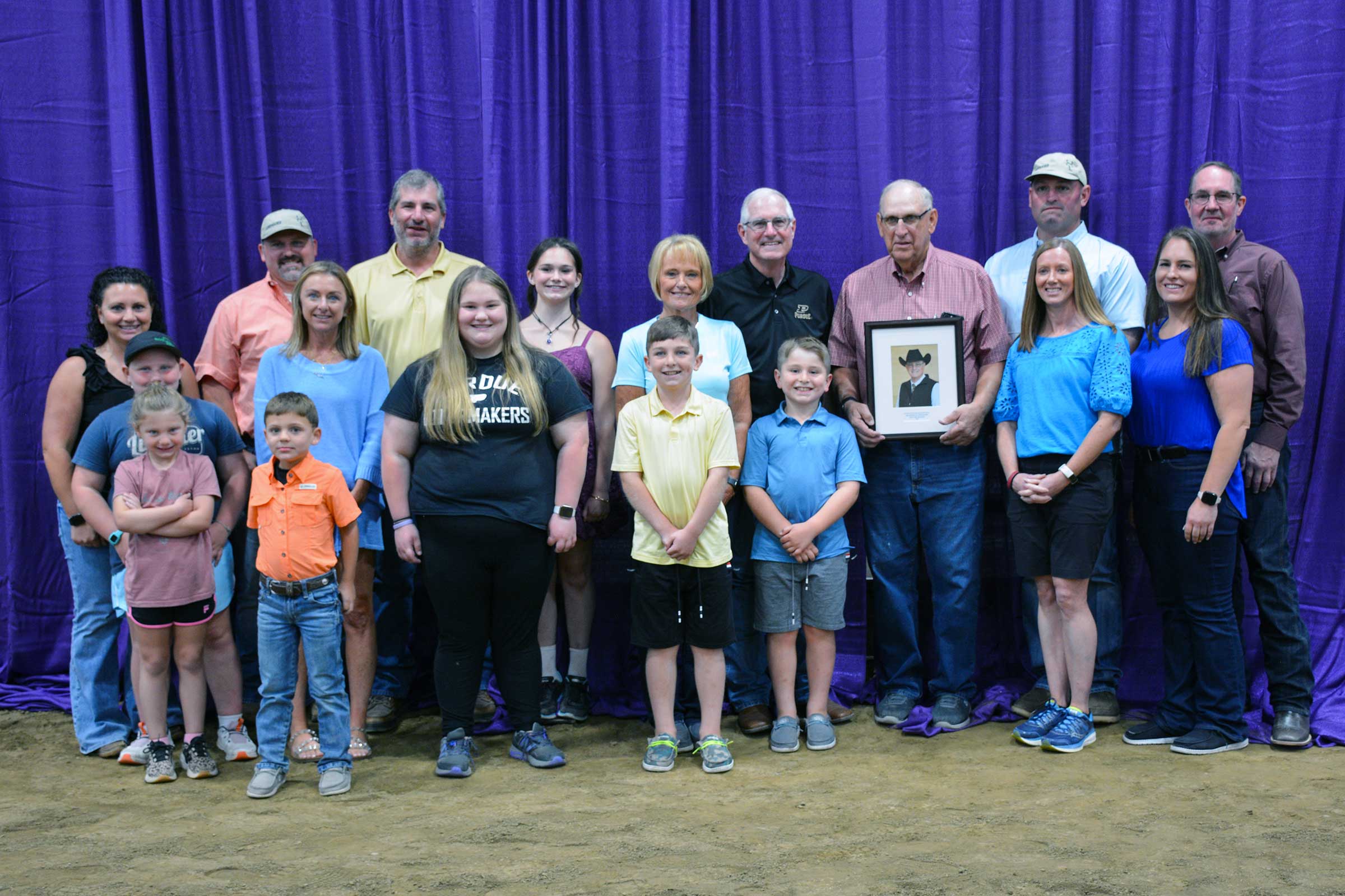 Ron Lemenager, Ph.D., joins family members and colleagues for a photo after his Indiana Livestock Breeders Association Hall of Fame induction at the Indiana State Fair, holding a framed portrait.