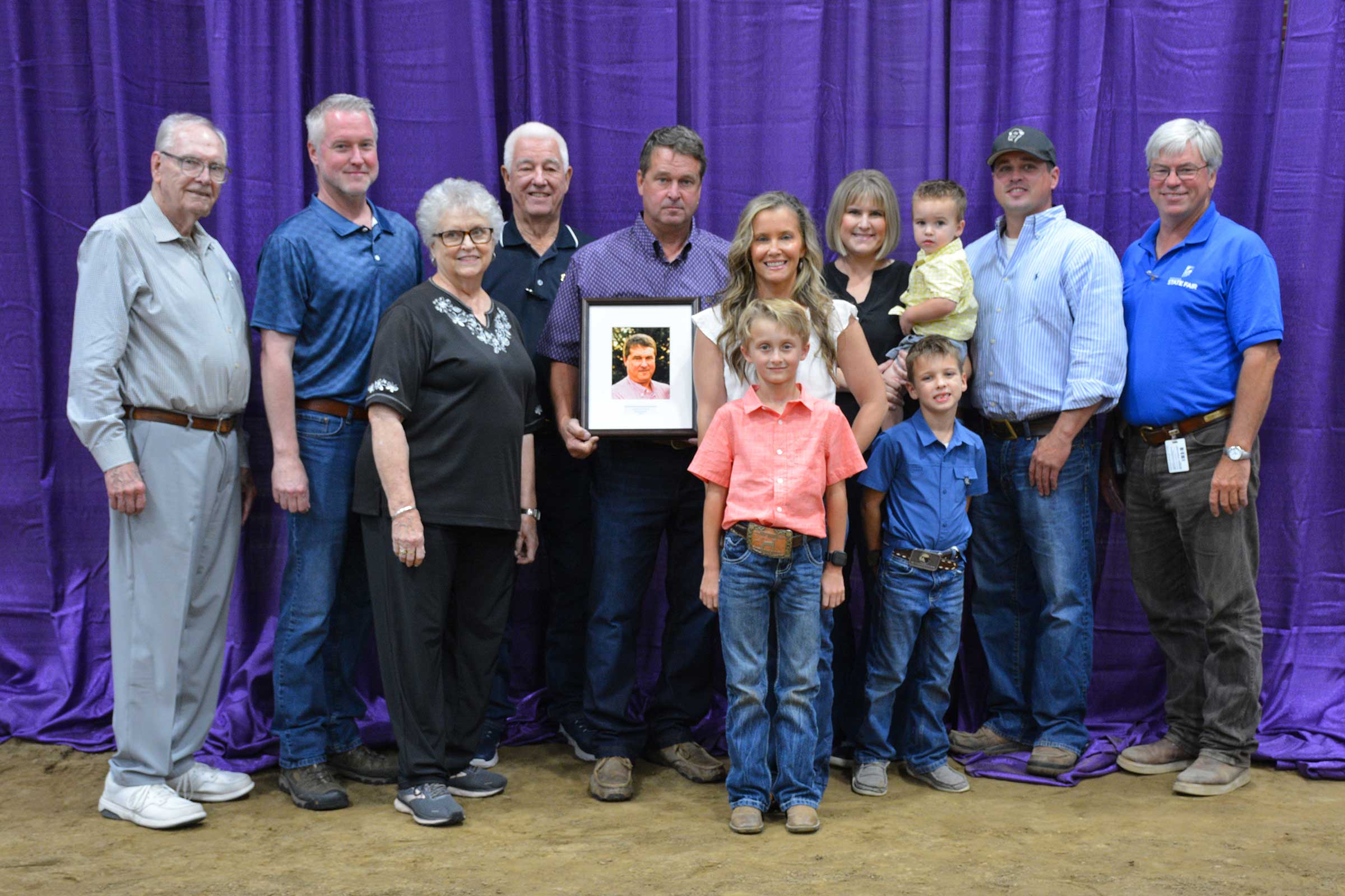 Stanley Poe II stands with his extended family, holding his Hall of Fame portrait after being inducted into the Indiana Livestock Breeders Association Hall of Fame at the Indiana State Fair.