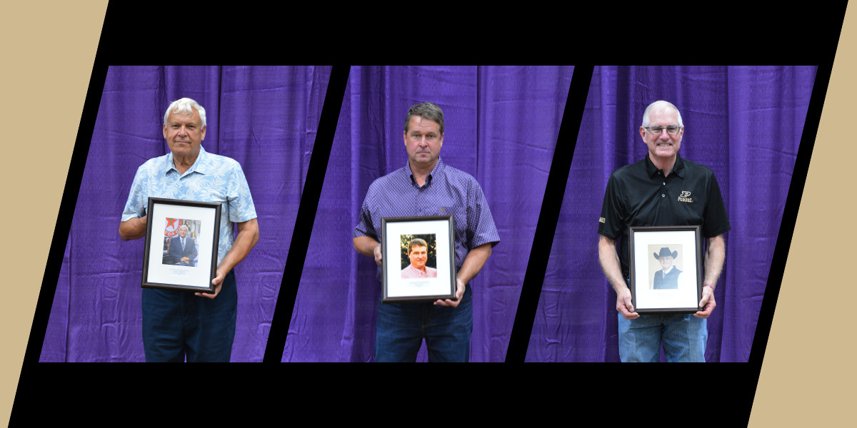Keith Lambright, Stanley Poe II, and Ron Lemenager, Ph.D., holding framed portraits after their induction into the Indiana Livestock Breeders Association Hall of Fame at the Indiana State Fair. They stand in front of a purple backdrop.