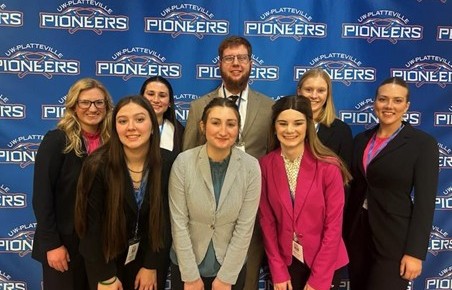 Eight Purdue Dairy Club students stand in front of a University of Wisconsin–Platteville Pioneer backdrop at the Midwest ADSA-USD annual meeting.
