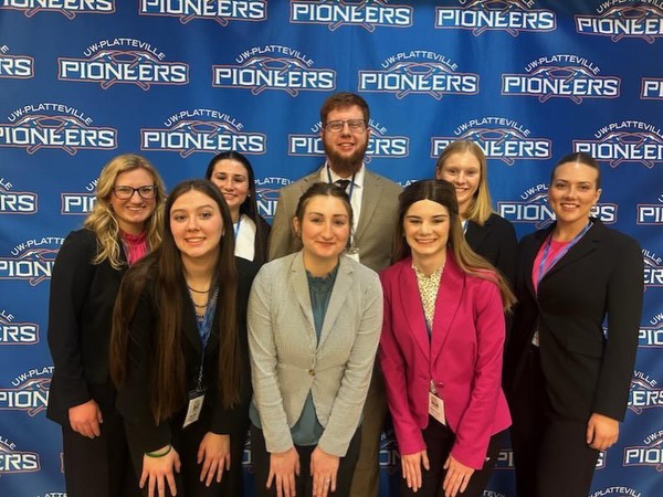 Eight Purdue Dairy Club students pose in front of a University of Wisconsin–Platteville Pioneer backdrop at the Midwest ADSA annual meeting.