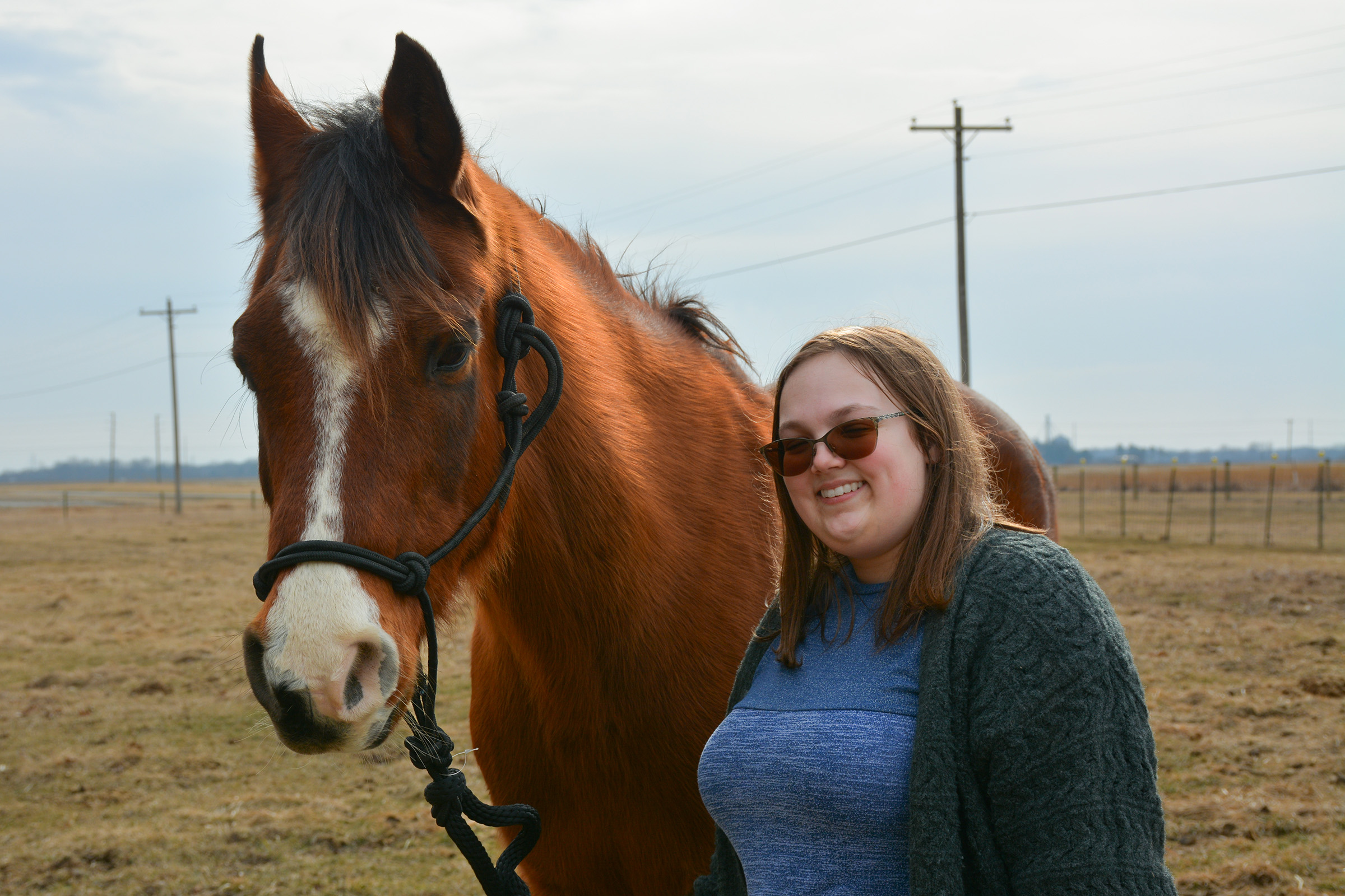 A student stands next to a horse.