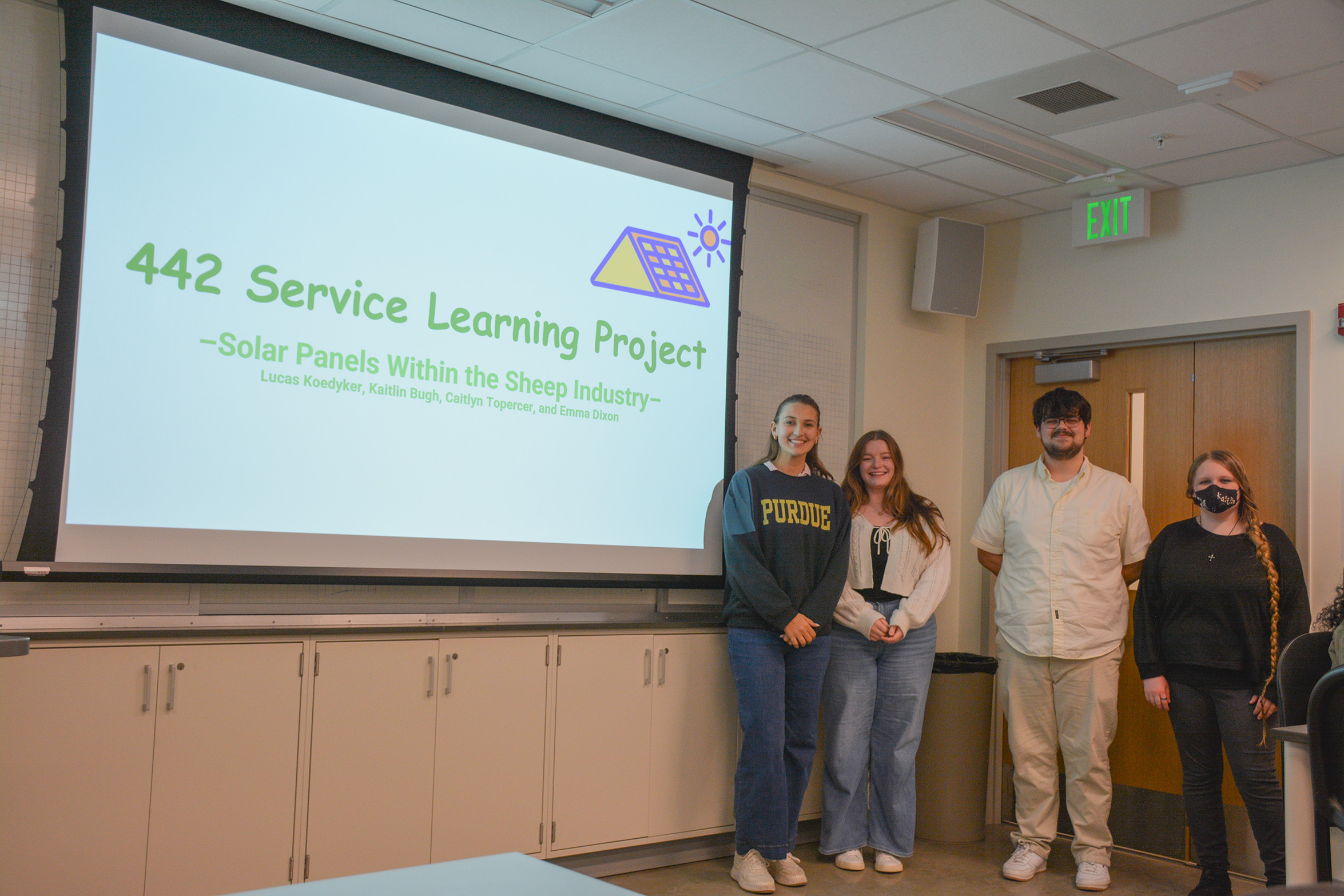 Students stand in front of a presentation that's titled "Solar Panels within the Sheep Industry."