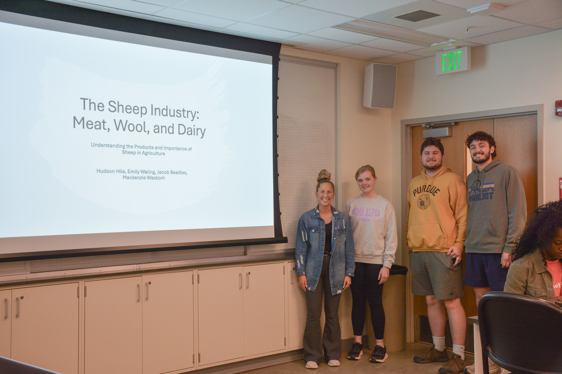 Students stand in front of a presentation that's titled "The Sheep Industry: Meat, Wool, and Dairy."