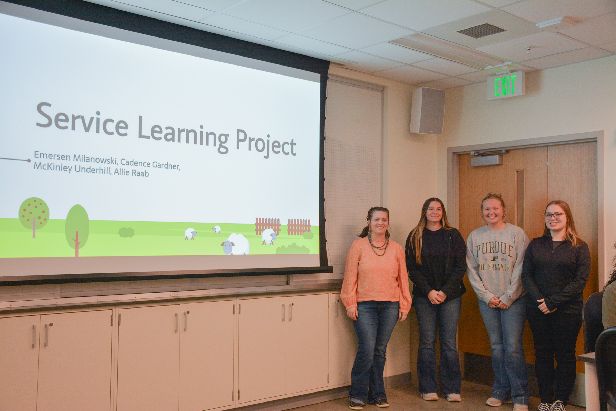 Students stand in front of a presentation titled "Service Learning Project."