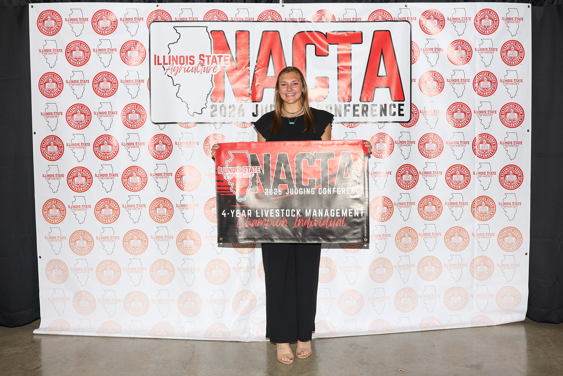 Grace Kreischer holds a NACTA 2026 Judging Conference 4-Year Livestock Management Champion Individual banner.