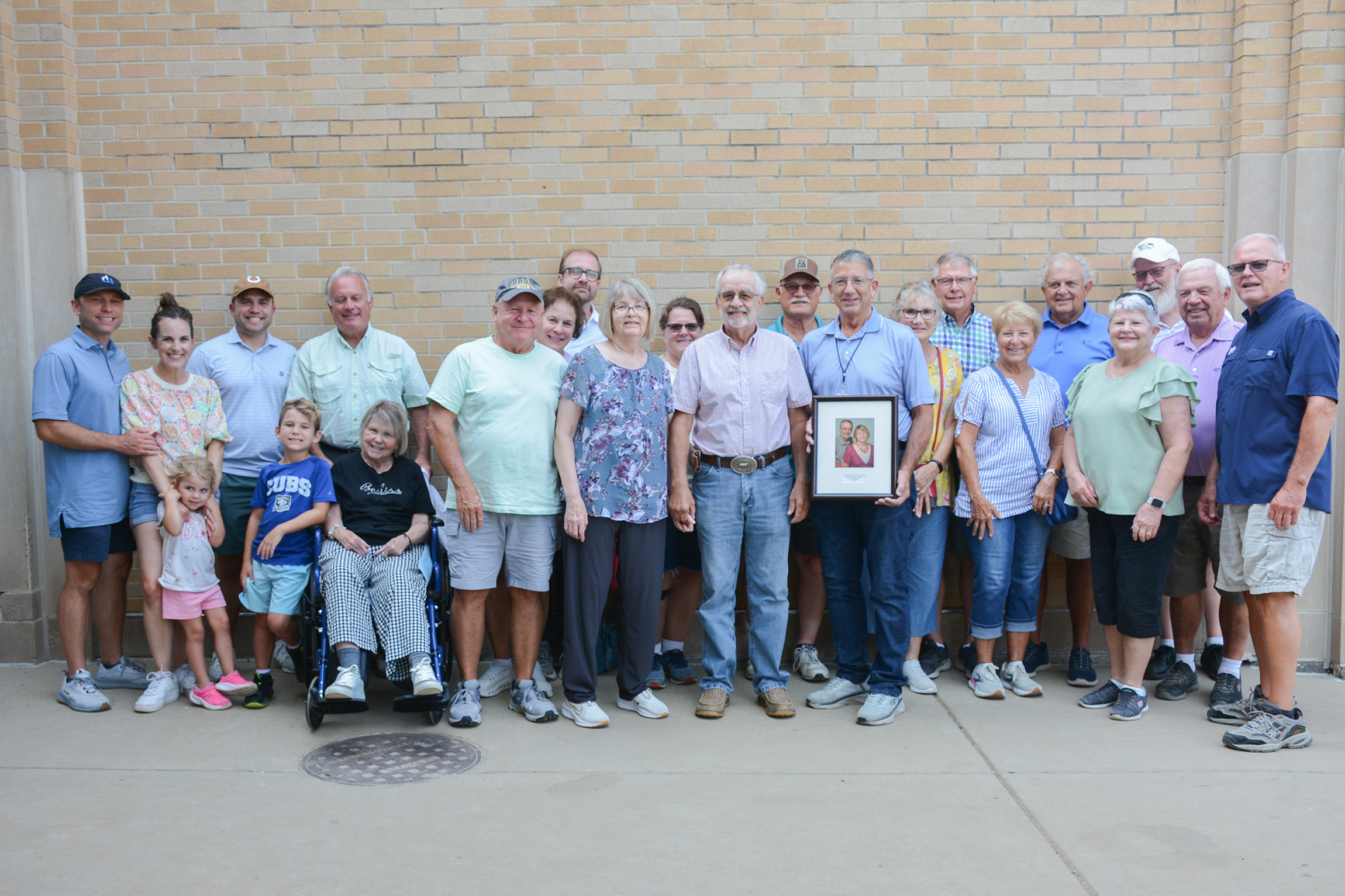 Larry and Janet White and their friends and family stand together in front of a brick wall.
