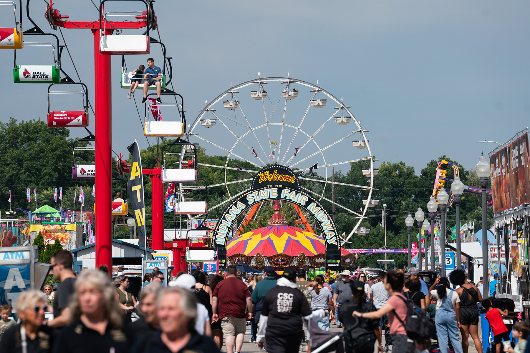 The state fair midway, featuring crowds of people and a ferris wheel.