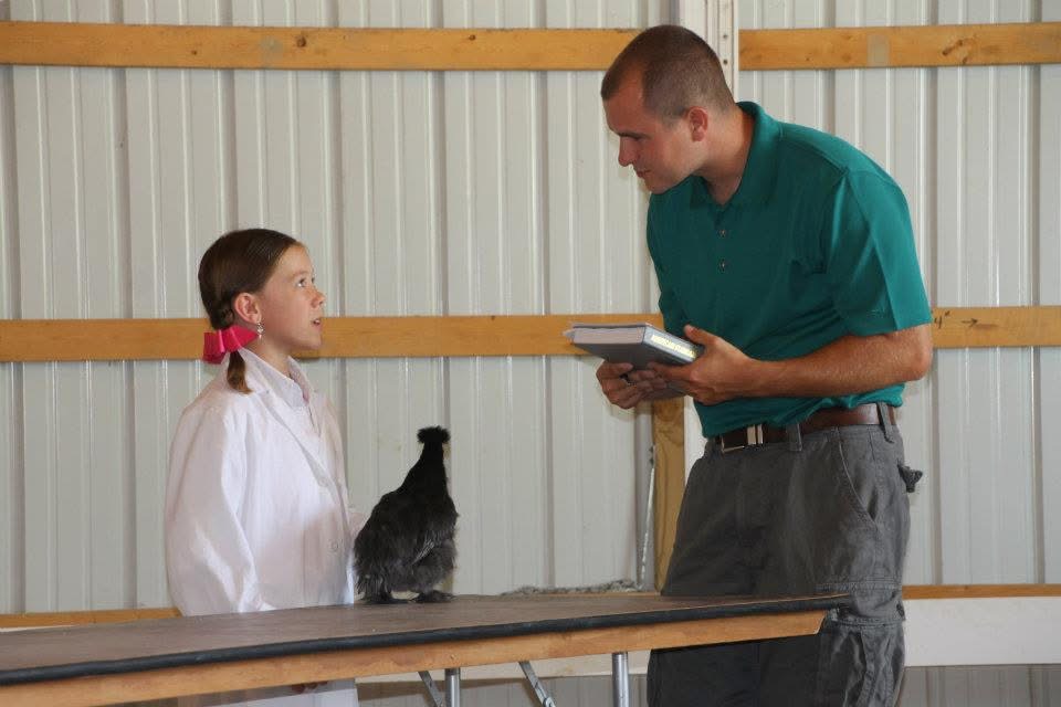 Isabella von Seggern shows a chicken in 4-H, and a judge stands nearby.
