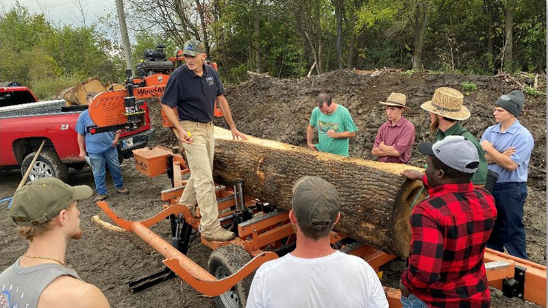 Dr. Rado Gazo teaching Hardwood University workshop standing over a log with class listening in forest.