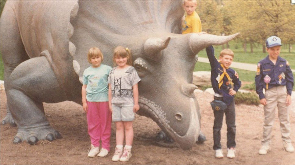 Geriann Albers stands next to a statue of a triceratops as a child.