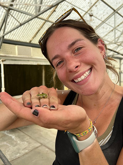 Kadian holds a small frog found in the greenhouse. Frogs are actually beneficial in the greenhouse because they eat fungus gnats which can damage roots of seedlings. 