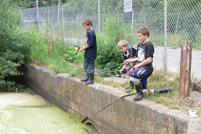 Dr. Zackary Delisle standing on a concrete wall, fishing with his brothers as a child. 