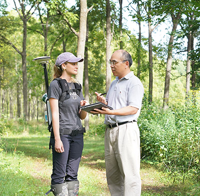 Dr. Songlin Fei and a female student look at digital forestry data on a tablet in the woods