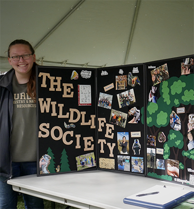 Alex Dudley stands next to a Purdue student chapter of The Wildlife Society booth