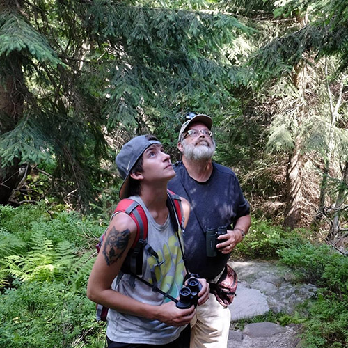 Dr. Barny Dunning birding with Ashley Higdon; Dr. Barny Dunning holds binoculars on a trip to the Pacific Northwest; Dr. Barny Dunning with Tam Tran atop a mountain in Costa Rica