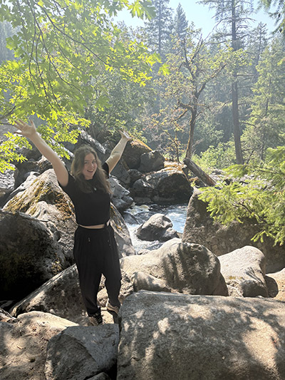 Alexandra Early standing in front of water flowing through the Avenue of Boulders in Prospect, Oregon