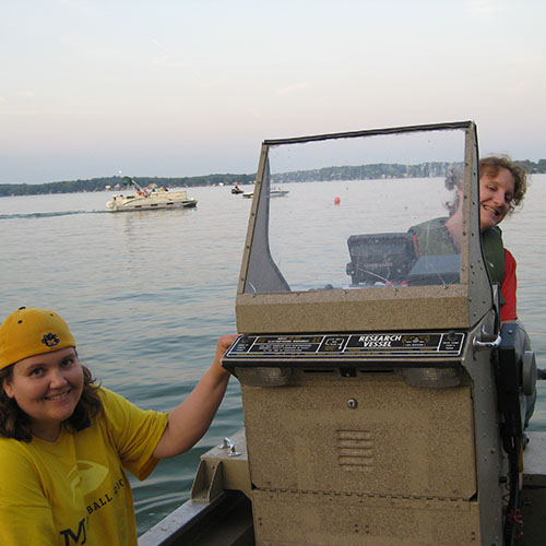 Carolyn Foley drives a boat with a University of Michigan Student