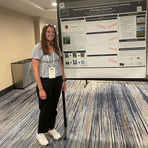 A cover crop dominated by red clover in the inter-row of a vineyard, which provides nesting resources for birds and flowers for pollinators; Sarah Grimes stands next to an automated recording unit at a vineyard in northern Michigan.