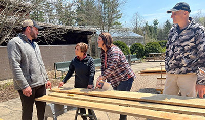 Students at the Introduction to Hardwood Lumber Grading class measure and look at a piece of lumber with Dr. Rado Gazo (right) looking on