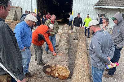 Students at a log bucking class look on as one man sprays orange paint on a log