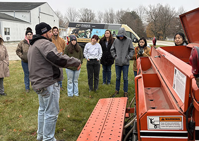 The Indiana LSLA group talks with a local farmer in front of farm equipment.