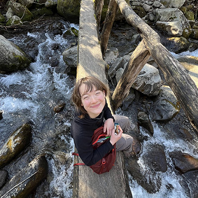 Alyssa Johnson sits on a log with water flowing underneath