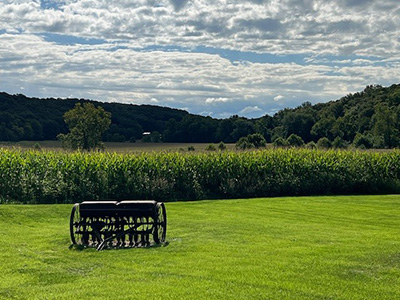 The Milnes Family Farm with a piece of antique farm equipment, a field and forest land