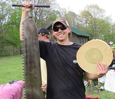 Sam Goedde holds a saw and a wood cookie at Midwest Conclave 2026