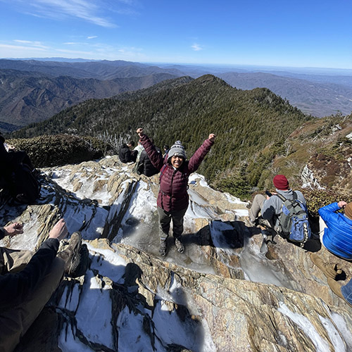 Gabby Dennis raises her hands above her head in celebration after summiting Mount Le Conte. 