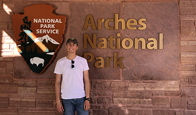 Zane Smoldt stands next to the sign for Arches National Park