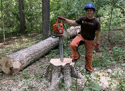 Andrew Tucker holds a chainsaw near a tree he felled as part of timber stand improvement work.