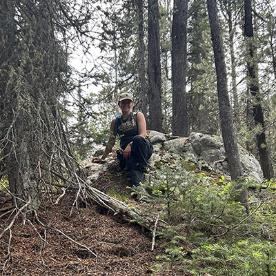 Lauren Wetterau kneels next to a red squirrel midden. 