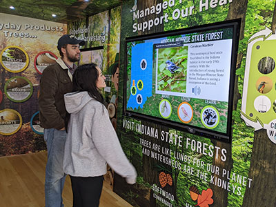 Two people look at part of the Woods on Wheels exhibit about forest management