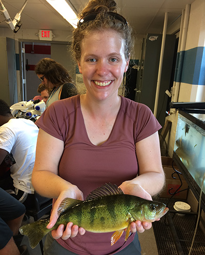 A picture of Zoe Almeida holding a yellow perch collected off Stone Lab during her PhD work.