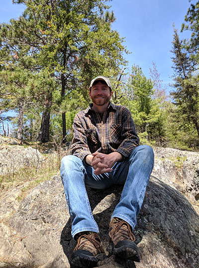 Travis Stoelting sits on a rock in front of forest land