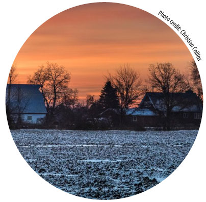 snow covered farm field at sunset with a barn and house on the horizon. Credit: Christian Collins